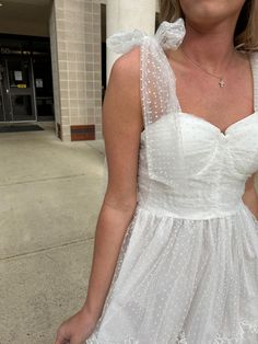 a woman in a white dress standing on the sidewalk