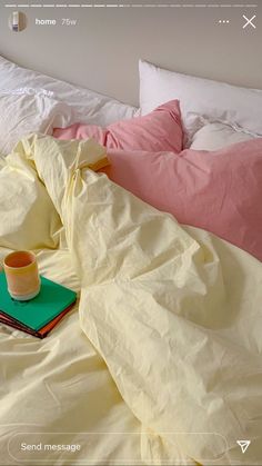 a book and cup are sitting on a bed with white sheets, pillows and blankets