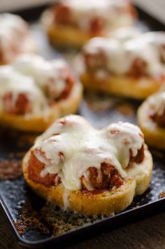 mini pizzas with meat and cheese are on a baking sheet