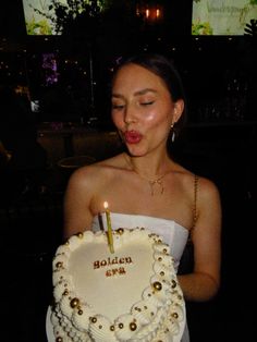 a woman blowing out the candles on her birthday cake that is shaped like a heart