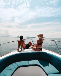 two women in bikinis sitting on the back of a boat looking out to sea