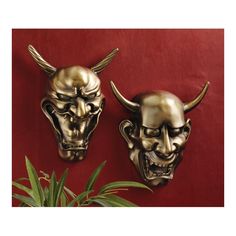 two gold masks on a red wall next to a potted plant