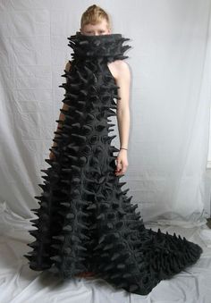 a woman is standing in front of a white backdrop wearing a black dress with spikes on it