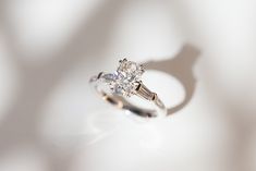 a diamond ring sitting on top of a white surface with light coming through the background