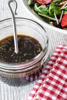 a salad in a jar next to a bowl with dressing on it and a red checkered napkin