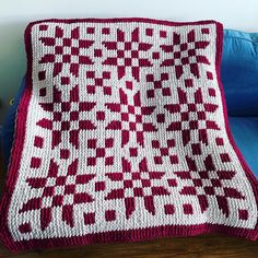 a red and white crocheted blanket sitting on top of a blue couch next to a pillow