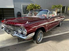 an old red car is parked in front of a building with palm trees on the sidewalk