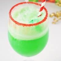 a green and red drink with a straw in it's glass next to some candy