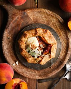 an apple pie is on a plate with spoons next to it and some sliced peaches