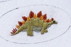 a small embroidered brooch with an orange and yellow flowered dinosaur on it's back