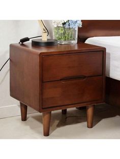 a night stand with two drawers and a lamp next to it on top of a bed