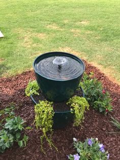 a water fountain surrounded by plants and mulch