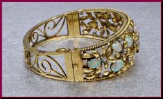 "Bold and beautiful, this 1950's vintage bangle is set in 14k yellow gold. Within the gold roped frame are golden flowers with round diamond centers. The drama comes in with 11 large fiery oval opals thriving between the gold flowers. A look of relentless pizzazz. The bangle will fit a large wrist. The inside circumference is 7 ¼\". It weighs 46.62 grams. BR 447 SIX MONTH LAY-AWAY AVAILABLE - PLEASE CONTACT ME TO SET UP A PLAN" Opal Bangle, Solid Gold Bangle, Garnet Wedding, Ruby Bangles, Yellow Gold Bangle, Gemstone Bangle, Vintage Bangles, Six Month, Diamond Cocktail Rings