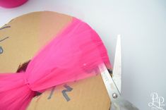 a pair of scissors cutting through a piece of cardboard with pink tulle on it