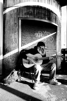 a man sitting on a bench with a guitar in front of a building that has graffiti all over it