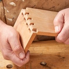 a person holding a wooden object in their hands on top of a piece of wood