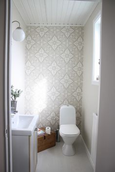 a white toilet sitting next to a sink in a bathroom under a window with light coming through