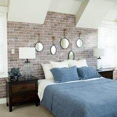 a bedroom with three mirrors on the brick wall above the bed and two night stands