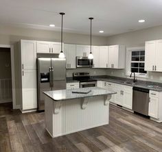 a large kitchen with white cabinets and stainless steel appliances, along with hardwood flooring