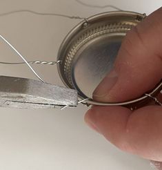 a hand holding a piece of metal wire with a pair of scissors attached to it