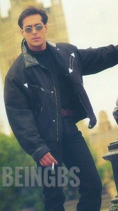 a man in black jacket and sunglasses standing next to a fountain with a clock tower in the background