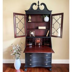 an old fashioned desk and hutch in a room with wood floors, vases and mirror on the wall