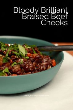 a blue bowl filled with meat and vegetables on top of a white table next to a fork