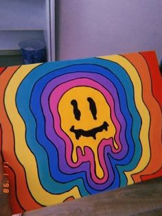 a person holding up a colorful painting with a smiley face on it's side