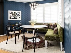 a dining room with blue walls and white trim on the ceiling, green chairs around a round table