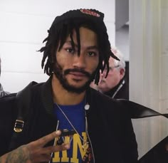 a man with dreadlocks and a blue t - shirt is pointing at something