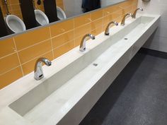 a row of sinks in a public restroom with urinals on the wall behind them