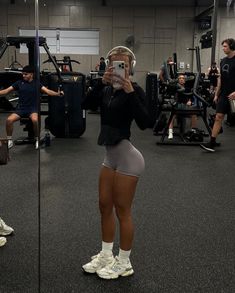 a woman in grey shorts and headphones standing next to a mirror with other people behind her