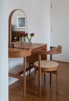 a wooden desk with a mirror, chair and vase on it in a white room