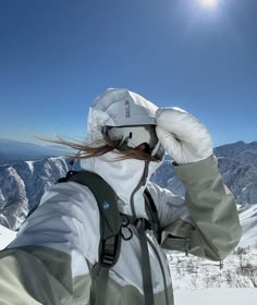 a person with long hair standing on top of a snow covered slope wearing skis