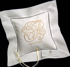 a white pillow with embroidered monogrammed initials on it and a gold ribbon around the edge