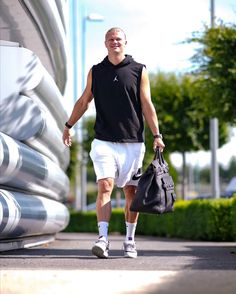 a man is walking down the street carrying a black bag and wearing white shorts with his foot in the air