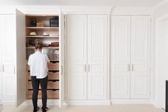 a woman standing in front of a white closet filled with lots of drawers and cupboards