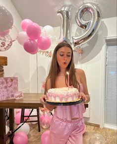 a woman in pink is holding a cake with a candle on it and balloons around her