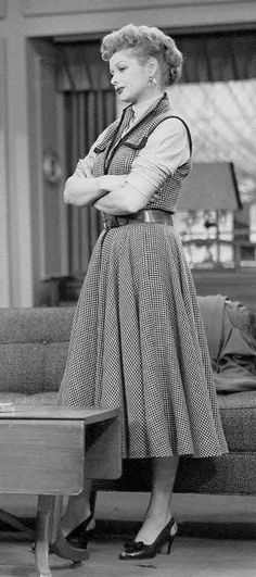 an old woman standing in front of a couch with her arms crossed and looking off to the side