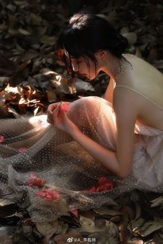 a woman in a white dress is sitting on the ground with leaves and petals around her