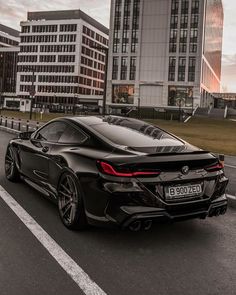 a black sports car driving down the road in front of some tall buildings at sunset