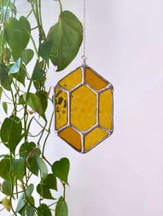 a yellow and silver hexagon hanging from a plant with green leaves on it