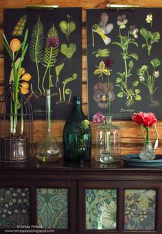 vases with flowers and plants are sitting on a table in front of two paintings