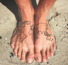 two people with tattoos on their feet standing in the sand