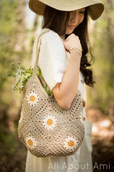 a woman wearing a hat and holding a crocheted bag with daisies on it