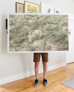 a person holding up a large poster with grass on it's side in front of a wooden floor