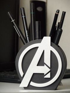 an avengers logo pen holder with pens and pencils in it sitting on a desk