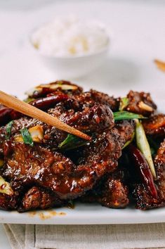 a plate full of food with chopsticks sticking out of the meat and vegetables