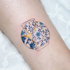 a blue and white vase tattoo on the left arm with gold scissors sticking out of it