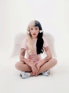 a woman with long hair sitting on the ground in front of an angel wings background